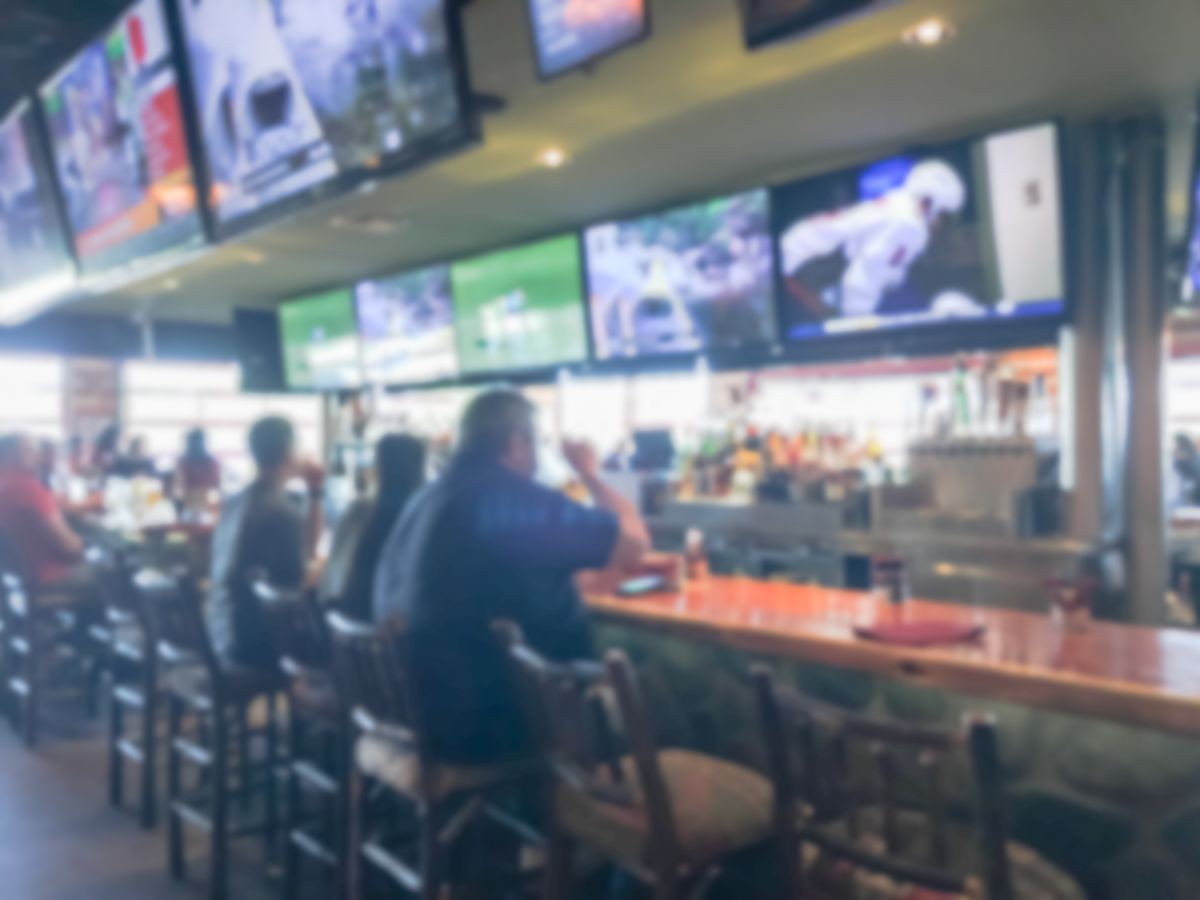 Blurred abstract sports bars and restaurants in America. People drink craft beer, hanging out, resting, watching sport. Large wall mount flat-screen TV, classic wooden table, chair, Happy Hour concept